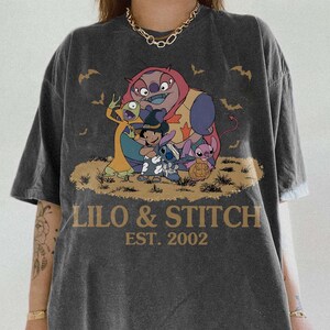 Op de afbeelding: Donkergrijs T-shirt met een afbeelding van Lilo & Stitch-personages en de tekst "LILO & STITCH EST. 2002". Het shirt heeft een vintage uitstraling en het Comfort Colors Pepper-logo.