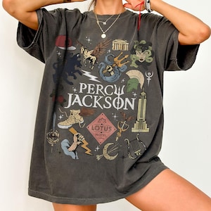以下が含まれることがあります： Percy JacksonとLotus Hotelの文字がプリントされたチャコールグレーのオーバーサイズTシャツ。デザインには、翼のある馬、三叉の矛、ギリシャの兜、竪琴、エンパイアステートビルなど、さまざまなイラストが描かれています。