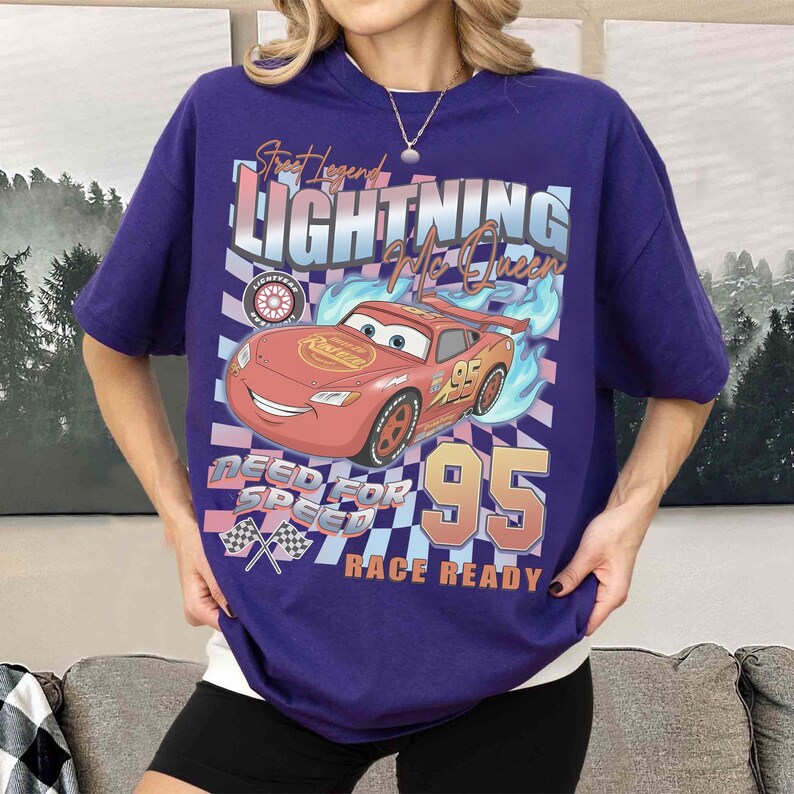 May include: A purple t-shirt featuring Lightning McQueen from the Cars movie. The graphic includes the text "Street Legend Lightning McQueen" and "Need for Speed Race Ready" with a checkered flag design. The number 95 is also prominently displayed.