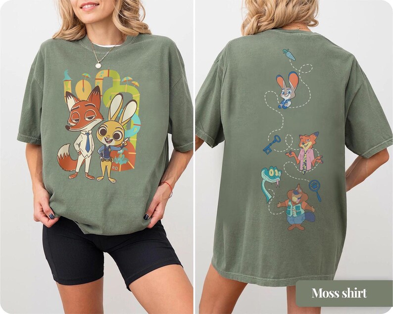 May include: A moss green t-shirt featuring a cartoon fox and rabbit with the text "100". The back of the shirt has additional cartoon characters and objects. The shirt is made of a soft material.