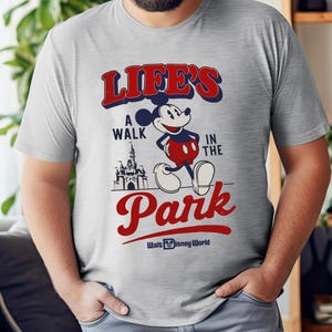 Puede incluir: Camiseta gris claro con Mickey Mouse y el texto "LIFE'S A WALK IN THE PARK" en rojo y azul. El dise&ntilde;o incluye un castillo y las palabras "Walt Disney World" en blanco.
