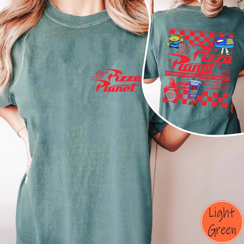 Puede incluir: Camiseta verde claro con el logo rojo "Pizza Planet" en la parte delantera. La parte trasera presenta un dise&ntilde;o a cuadros rojos y blancos con personajes de dibujos animados y texto. La camiseta es de material suave.