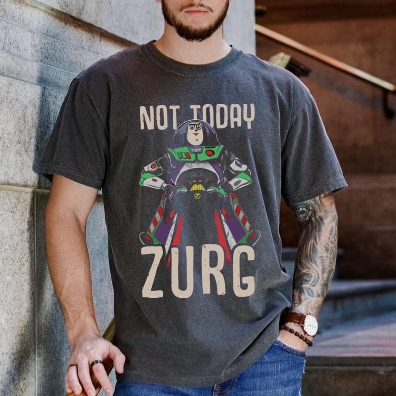 Op de afbeelding: Donkergrijs t-shirt met een afbeelding van Buzz Lightyear en de tekst "NOT TODAY ZURG". Het ontwerp bevat groene, paarse en rode accenten. Het shirt is gemaakt van een zacht, comfortabel materiaal.