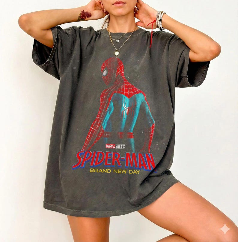 May include: Dark grey t-shirt with a Spider-Man graphic from Marvel Studios. The design shows the character in his red and blue suit, with the words "SPIDER-MAN BRAND NEW DAY" in red and blue text.