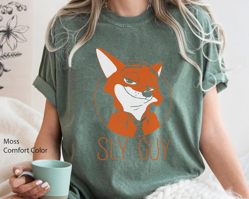 Puede incluir: Camiseta de color verde musgo con un zorro de dibujos animados naranja y el texto "SLY GUY". El zorro est&aacute; dentro de un c&iacute;rculo. La camiseta es de manga corta y cuello redondo.