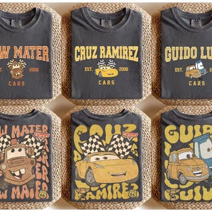 May include: Six charcoal gray t-shirts featuring designs from the Cars movie. Each shirt displays a different character's name in a vintage font, along with an image of the character and the text "Cars" and "EST. 2006".