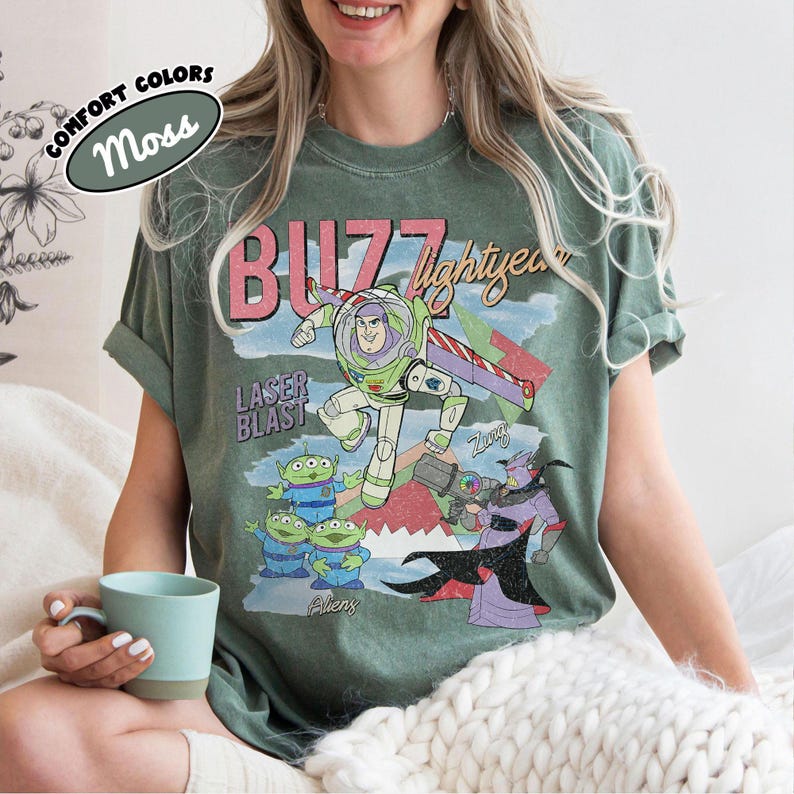 Puede incluir: Camiseta verde musgo con un gr&aacute;fico de Buzz Lightyear, el texto "Buzz Lightyear" y "Laser Blast". El dise&ntilde;o incluye extraterrestres y Zurg. La camiseta tambi&eacute;n tiene el texto "Comfort Colors".