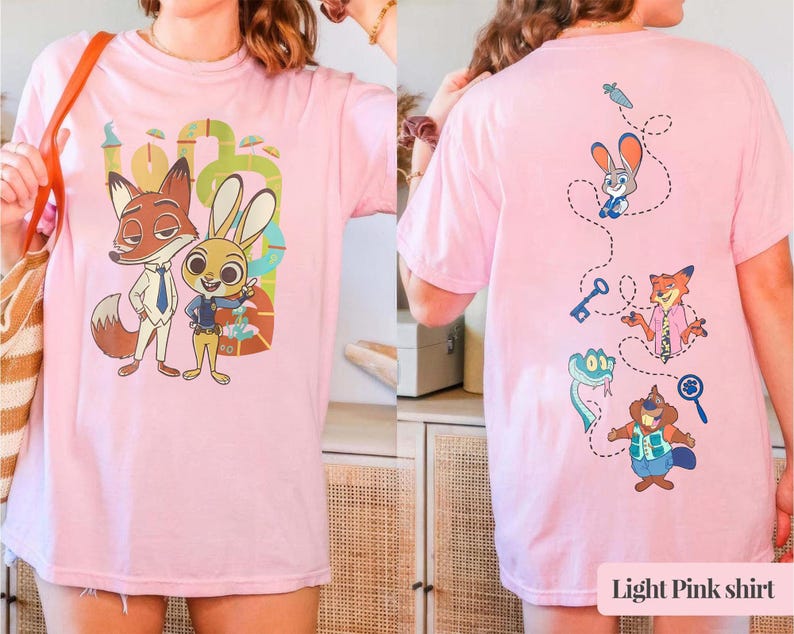May include: Pale pink t-shirt with Zootopia cartoon characters. The front shows Nick Wilde and Judy Hopps. The back has various characters with a carrot, key, and magnifying glass. The text "Light Pink shirt" is at the bottom.