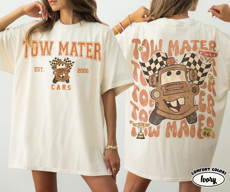 May include: Ivory-colored t-shirt featuring a distressed graphic of Tow Mater from the Cars movie. The front design includes the text "TOW MATER EST. 2006 CARS". The back design repeats "TOW MATER" with a cartoon image of Mater and checkered flags.
