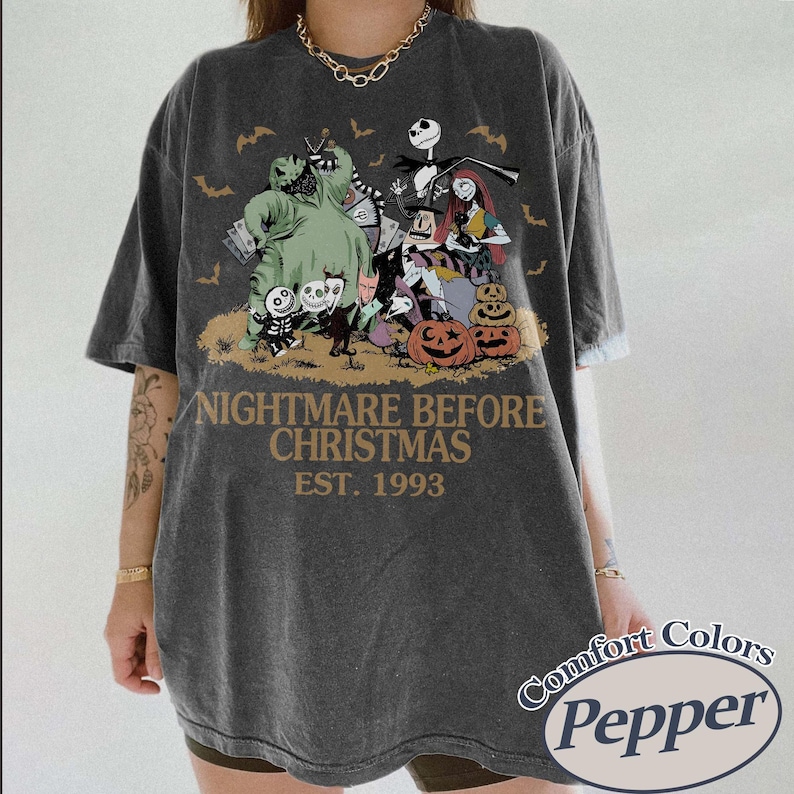 Puede incluir: Camiseta gris oscuro con un gr&aacute;fico de "Pesadilla antes de Navidad" con Jack Skellington, Sally y otros personajes. El texto "NIGHTMARE BEFORE CHRISTMAS EST. 1993" est&aacute; impreso debajo. La camiseta tiene una etiqueta Comfort Colors Pepper.