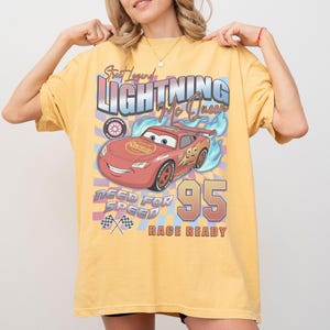 May include: Yellow t-shirt featuring a graphic of Lightning McQueen from the Cars movie. The design includes the text "Street Legend Lightning McQueen", "Need for Speed", and "Race Ready" with the number "95".