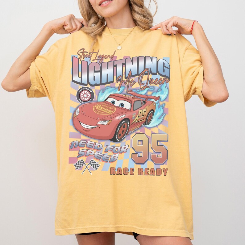 May include: Yellow t-shirt featuring a graphic of Lightning McQueen from the Cars movie. The design includes the text "Street Legend Lightning McQueen", "Need for Speed", and "Race Ready" with the number "95".