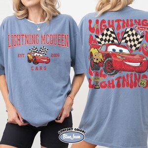 May include: A blue t-shirt featuring the text "LIGHTNING MCQUEEN" in red, with a graphic of the character Lightning McQueen and checkered flags. The back of the shirt has a larger graphic of Lightning McQueen and the words "LIGHTNING" and "CARS".