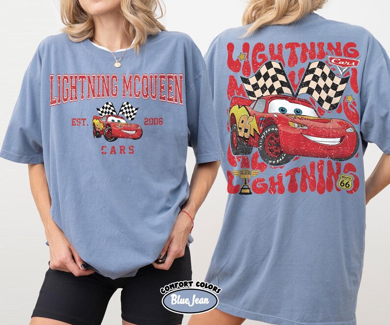 May include: A blue t-shirt featuring the text "LIGHTNING MCQUEEN" in red, with a graphic of the character Lightning McQueen and checkered flags. The back of the shirt has a larger graphic of Lightning McQueen and the words "LIGHTNING" and "CARS".