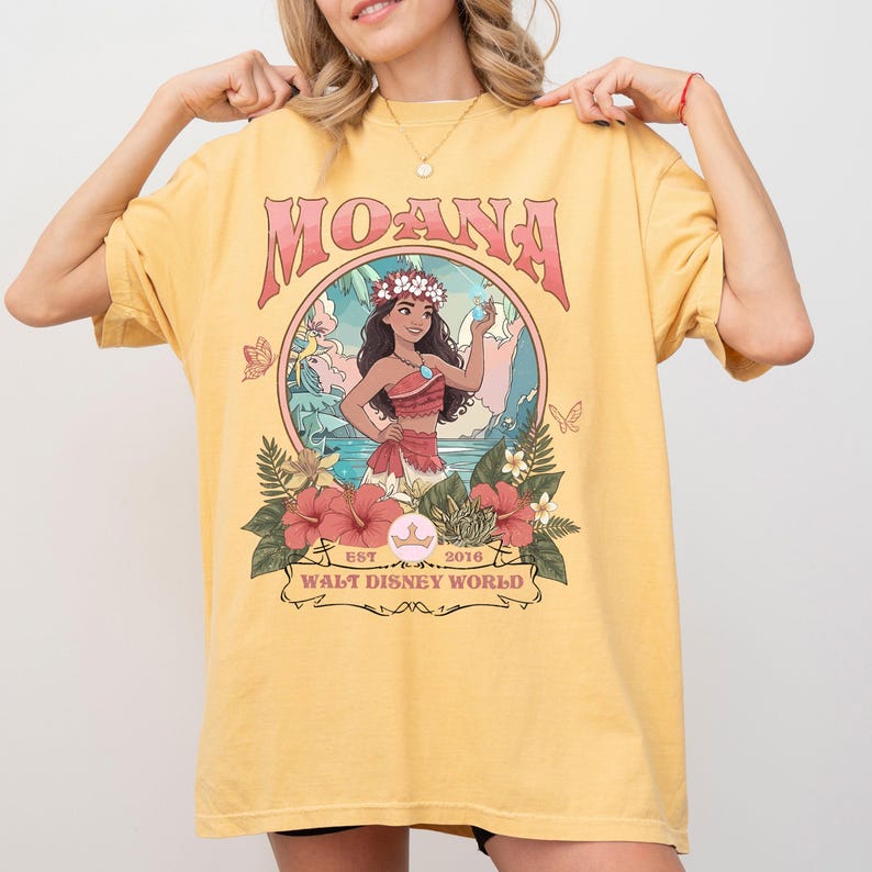 May include: Yellow t-shirt featuring a graphic of Moana, with the word "MOANA" in pink lettering. The graphic includes an illustration of Moana, flowers, and the text "EST. 2016 WALT DISNEY WORLD".