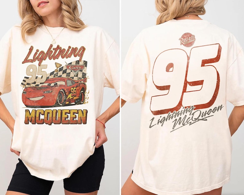 Op de afbeelding: Cr&egrave;mekleurig T-shirt met een versleten afbeelding van Lightning McQueen uit de film Cars. De voorkant toont het personage met de tekst "Lightning 95 McQueen". De achterkant heeft een grote "95" en de tekst "Lightning McQueen".