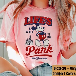 Puede incluir: Camiseta rosa claro con Mickey Mouse y el texto "LIFE'S A WALK IN THE PARK" en rojo y azul marino. El dise&ntilde;o incluye un castillo y "Walt Disney World".