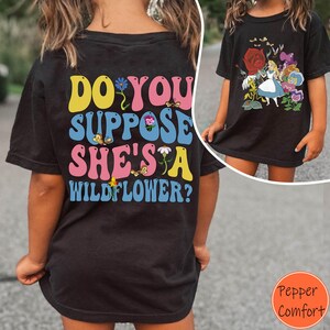 May include: Black t-shirt with the text "DO YOU SUPPOSE SHE'S A WILDFLOWER?" in yellow, pink, blue, and white. The shirt also features butterfly graphics. A second shirt shows a graphic of Alice in Wonderland with flowers.