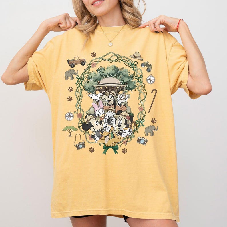 Puede incluir: Camiseta amarilla con un dise&ntilde;o de safari con Mickey Mouse, Minnie Mouse, Donald Duck, Goofy y Daisy Duck. El dise&ntilde;o incluye un jeep, una br&uacute;jula, unos prism&aacute;ticos y huellas de patas. Los personajes llevan sombreros de safari.