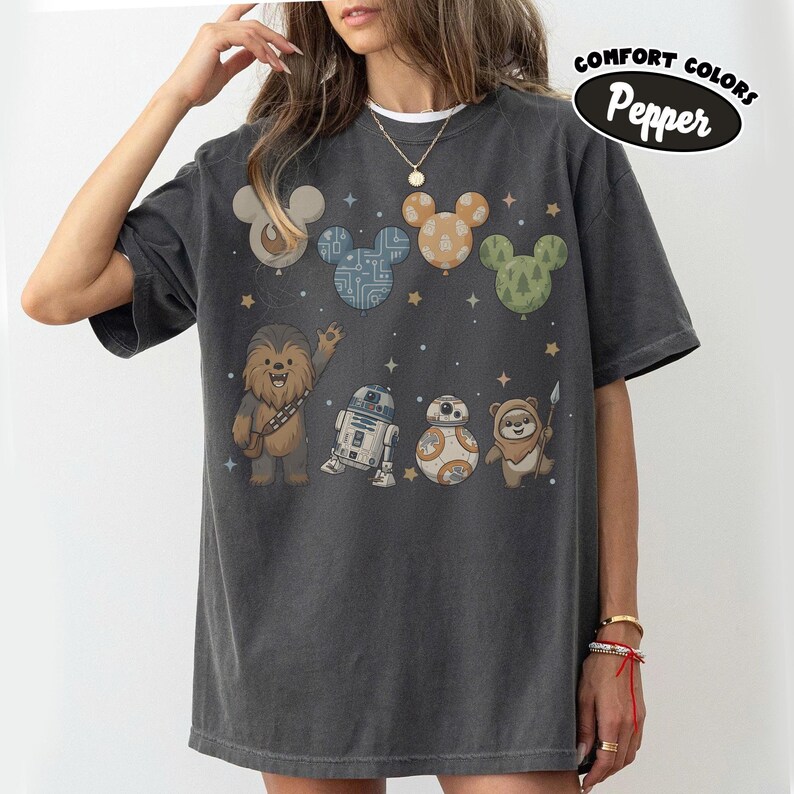 May include: Dark gray Comfort Colors t-shirt featuring a design with cartoon characters and Mickey Mouse ears. The design includes Chewbacca, R2-D2, BB-8, and an Ewok. The shirt also has the text "Comfort Colors Pepper" in a black oval.