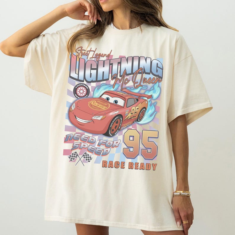 May include: Cream-colored t-shirt featuring a graphic of Lightning McQueen from the movie Cars. The design includes the text "Street Legend Lightning McQueen", "Need for Speed", and "Race Ready", along with the number 95.