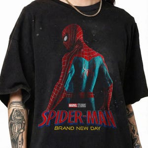 May include: Black t-shirt with a graphic of Spider-Man in a red and blue suit, the text "SPIDER-MAN" and "BRAND NEW DAY". The Marvel Studios logo is also visible on the shirt.