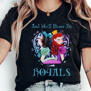 May include: Dark gray t-shirt featuring a graphic of two cartoon women with the text "And We'll Never Be ROYALS". The women are in a circular design with musical notes and floral accents. One woman has black hair and the other has red hair.