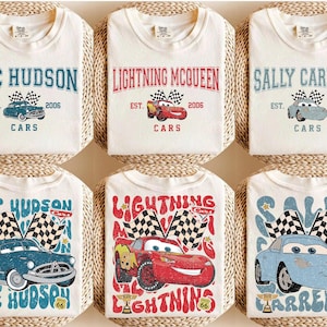 May include: Six white t-shirts featuring designs from the movie Cars. Each shirt displays a different character's name: Doc Hudson, Lightning McQueen, and Sally Carrera. The designs include the character's image, the year 2006, and the word "Cars".