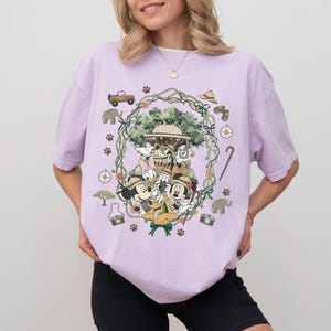 Puede incluir: Camiseta de color lila claro con un dise&ntilde;o tem&aacute;tico de safari que presenta a Mickey Mouse, Minnie Mouse, Donald Duck y Goofy. El dise&ntilde;o incluye veh&iacute;culos de safari, br&uacute;julas y huellas de patas. La camiseta tiene cuello redondo y mangas cortas.