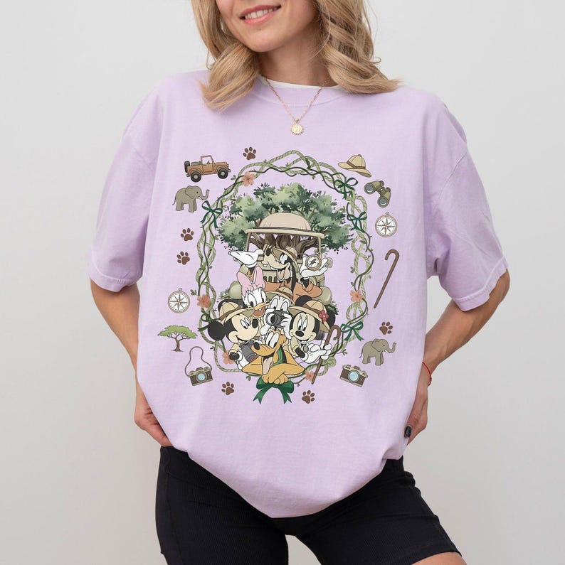 Puede incluir: Camiseta de color lila claro con un dise&ntilde;o tem&aacute;tico de safari que presenta a Mickey Mouse, Minnie Mouse, Donald Duck y Goofy. El dise&ntilde;o incluye veh&iacute;culos de safari, br&uacute;julas y huellas de patas. La camiseta tiene cuello redondo y mangas cortas.