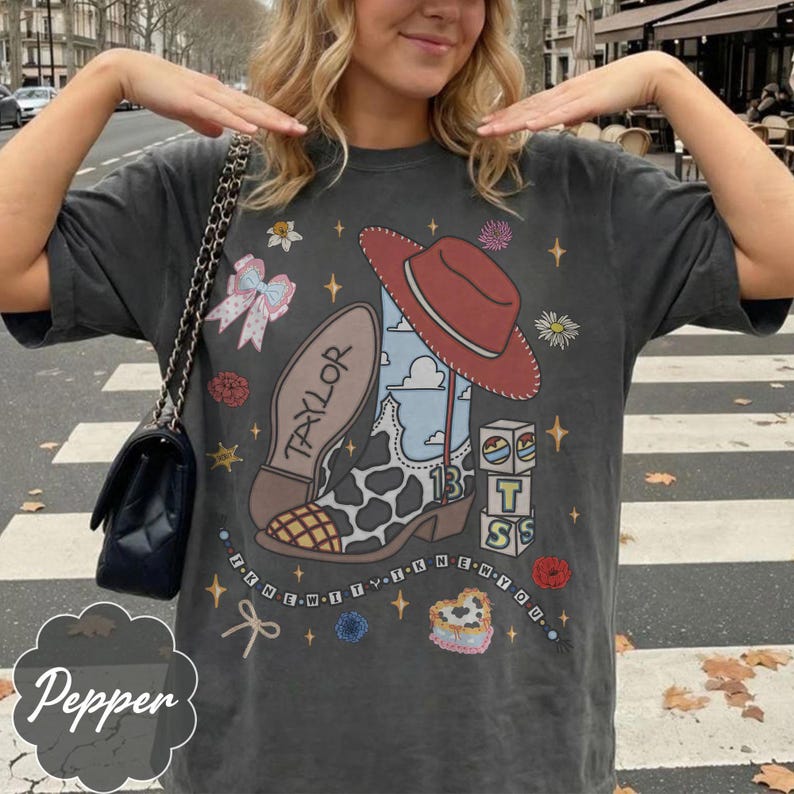 Peut inclure: Un t-shirt gris anthracite &agrave; manches courtes avec une impression graphique repr&eacute;sentant une botte de cow-boy &agrave; motifs de vache avec le nom Taylor, un chapeau de cow-boy rouge, des blocs avec le chiffre 13, un n&oelig;ud et le texte I KNEW IT I KNEW YOU.