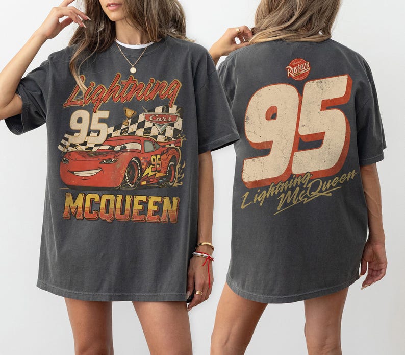 Op de afbeelding: Donkergrijze Lightning McQueen T-shirt. De voorkant heeft een afbeelding van de rode raceauto met nummer 95, een geblokte vlag en de tekst "McQueen". De achterkant toont een groot nummer 95 en de tekst "Lightning McQueen".