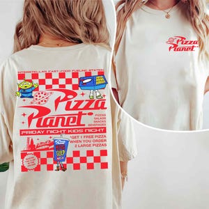 Puede incluir: Camiseta de color crema con el logo de Pizza Planet en la parte delantera y un gr&aacute;fico m&aacute;s grande en la parte trasera. El gr&aacute;fico trasero incluye el logo de Pizza Planet, personajes alien&iacute;genas y texto que promociona pizzas, snacks y bebidas.
