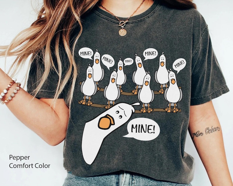 May include: Pepper Comfort Color t-shirt featuring a cartoon of seagulls on a wooden beam, each with a speech bubble saying "MINE!". One seagull is upside down with a speech bubble saying "MINE!".