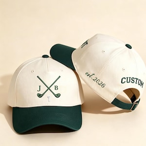 Puede incluir: Dos gorras de béisbol color crema y verde oscuro. La gorra frontal presenta palos de golf cruzados bordados con las letras J y B y un tee de golf. La gorra lateral muestra el texto bordado est. 2026 y la palabra CUSTOM en hilo verde oscuro.