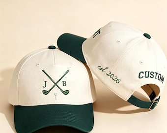 May include: Two cream and dark green baseball caps. The front cap features embroidered crossed golf clubs with the letters J and B and a golf tee. The side cap displays the embroidered text est. 2026 and the word CUSTOM in dark green thread.