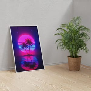 May include: A framed art print featuring a retro sunset scene with palm trees. The artwork showcases a vibrant pink and purple sun, blue water, and a dark blue sky. The print is displayed on a wooden floor next to a potted plant.