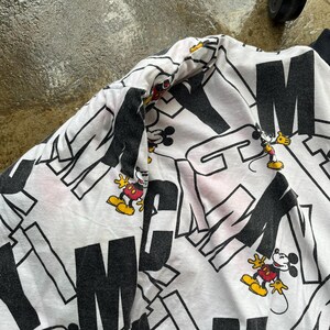 May include: White sweatshirt with a black and white graphic pattern featuring the letters "M" and "N" and cartoon images of Mickey Mouse. The sweatshirt has a black collar and cuffs.