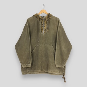May include: Olive green hooded anorak with a patterned hood and chest detail. The anorak has a front pocket, a half-zip closure, and a drawstring at the hem. The sleeves are long and loose, and the fabric appears to be a soft, textured material.