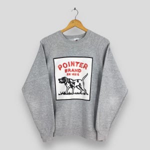 May include: A heather gray sweatshirt with long sleeves, featuring a graphic of a dog and the words "POINTER BRAND" in red. The dog is black and white, and the design is set within a white rectangle.