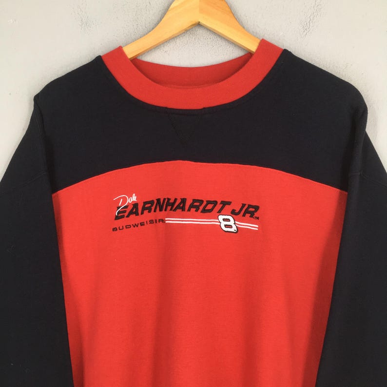 Puede incluir: Una sudadera negra, roja y blanca de Dale Earnhardt Jr. La sudadera tiene una secci&oacute;n superior y mangas negras, con un panel central rojo. El texto "Earnhardt Jr." y el n&uacute;mero "8" est&aacute;n impresos en la parte delantera.