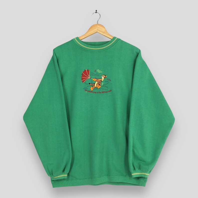 May include: Green sweatshirt with a cartoon tiger holding a red umbrella, with the text "It's a windy day in the 100 Acre Wood." The sweatshirt has yellow trim on the collar and cuffs.