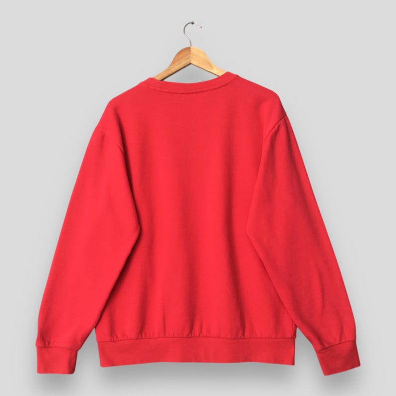 May include: A solid red sweatshirt hangs on a wooden hanger against a light gray background. The crew neck sweatshirt has long sleeves and ribbed cuffs and hem. The back of the sweatshirt is visible, showcasing its simple, clean design.