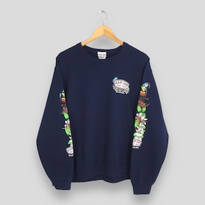 Puede incluir: Sudadera azul marino con cuello redondo. Las mangas presentan un dise&ntilde;o colorido de loros, flores y el texto "Ron Jon Surf Shop". Una versi&oacute;n m&aacute;s peque&ntilde;a del logotipo est&aacute; en la parte superior del pecho. La sudadera est&aacute; colgada de una percha de madera.
