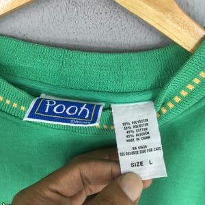 May include: Green Pooh sweatshirt with a yellow and white trim. The label reads "Pooh" with the Disney logo. The tag indicates the material is 55% polyester and 45% cotton. The size is Large.
