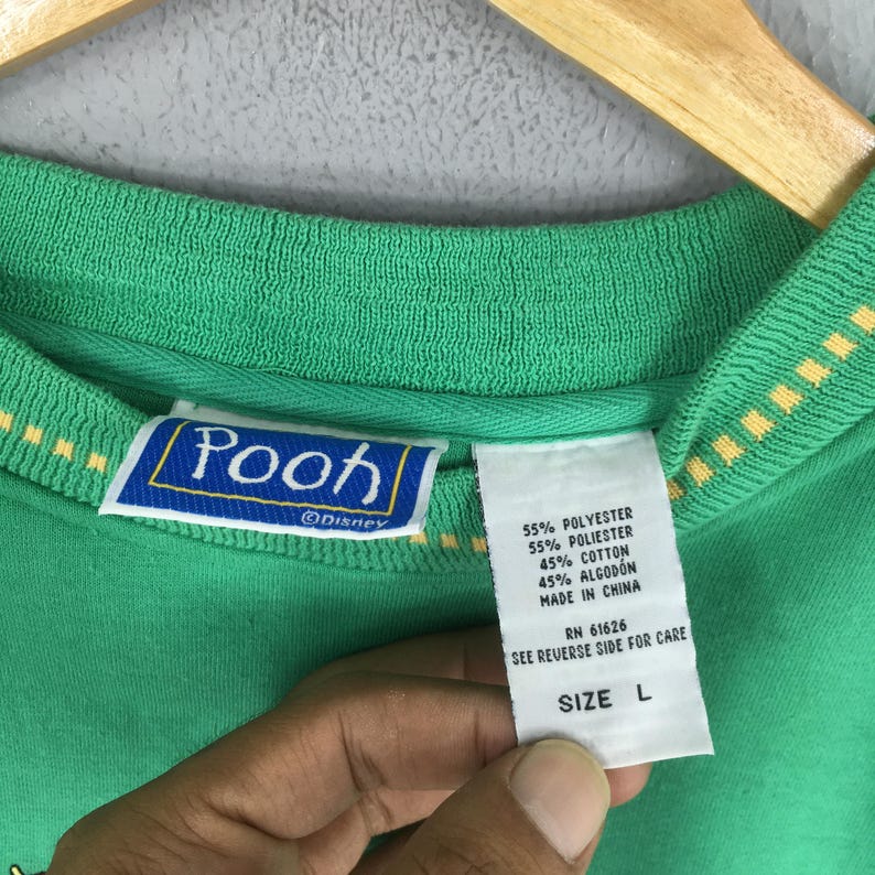 May include: Green Pooh sweatshirt with a yellow and white trim. The label reads "Pooh" with the Disney logo. The tag indicates the material is 55% polyester and 45% cotton. The size is Large.