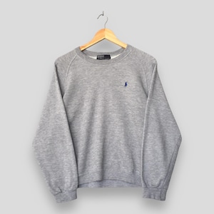 May include: A heather gray sweatshirt with a crew neck and long sleeves, hanging on a wooden hanger. A small blue logo is embroidered on the left chest. The sweatshirt is made of a soft, comfortable material.