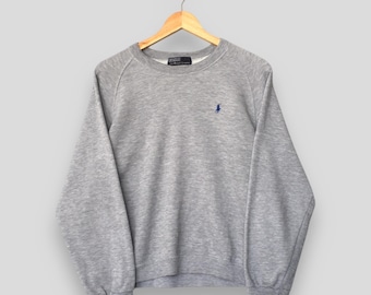 May include: A heather gray sweatshirt with a crew neck and long sleeves, hanging on a wooden hanger. A small blue logo is embroidered on the left chest. The sweatshirt is made of a soft, comfortable material.