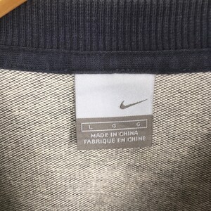 May include: Close-up of a gray and navy blue garment tag. The tag features the Nike swoosh logo and the text "MADE IN CHINA". The garment appears to be a sweatshirt or similar apparel item.