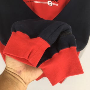 Puede incluir: Sudadera roja y azul marino con el n&uacute;mero 8 y texto. Los pu&ntilde;os y el dobladillo inferior son rojos, mientras que las mangas y la parte superior del cuerpo son azul marino. La sudadera est&aacute; hecha de un material suave y c&oacute;modo.